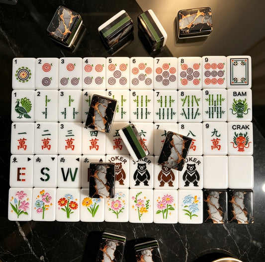 Overhead shot of scattered black gold marble mahjong tiles on gold tray, luxury black marble with gold foil backs, green striped edges, peacock tile and classic mahjong suit illustrations
