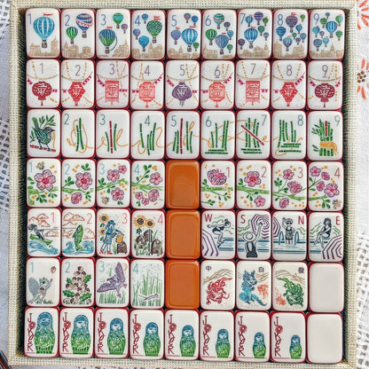 Rainbow Voyage Mahjong Tiles Set — Amber‑orange backs, multi‑layer rainbow striped sides, ivory fronts with hot‑air balloon, dragon, lantern, cherry‑blossom bee and matryoshka nesting‑doll joker American mahjong tiles