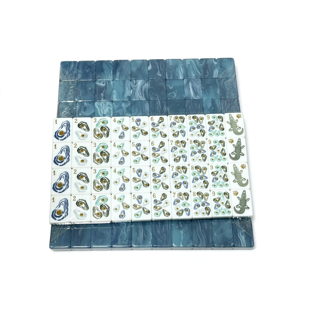 Oyster Bay coastal American mahjong set on white background, blue marbled tile backs stacked above white tile faces printed with oyster dots, heron bamboo, crab characters and alligator dragon tiles