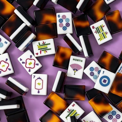 Close-up shot of tortoise pattern mahjong tiles on purple background, white tile faces with colorful hand-drawn flower, lantern, bamboo and fan NORTH wind artwork