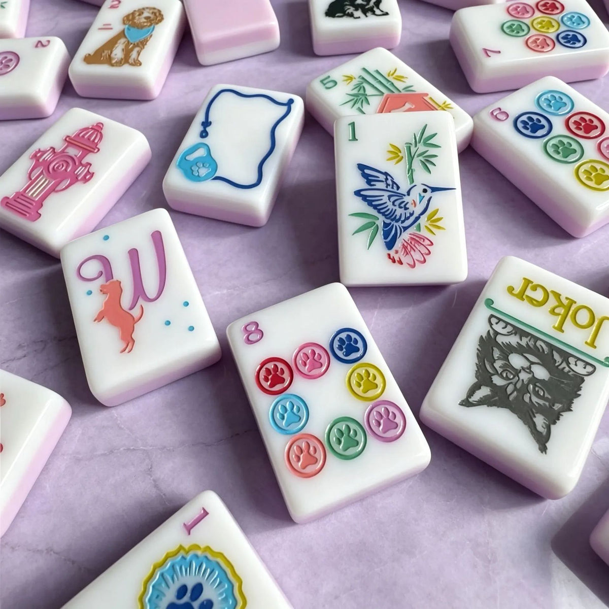 Close-up of pink solid mahjong tile backs stacked beside pet art mahjong tiles, paw print and award ribbon suit tiles