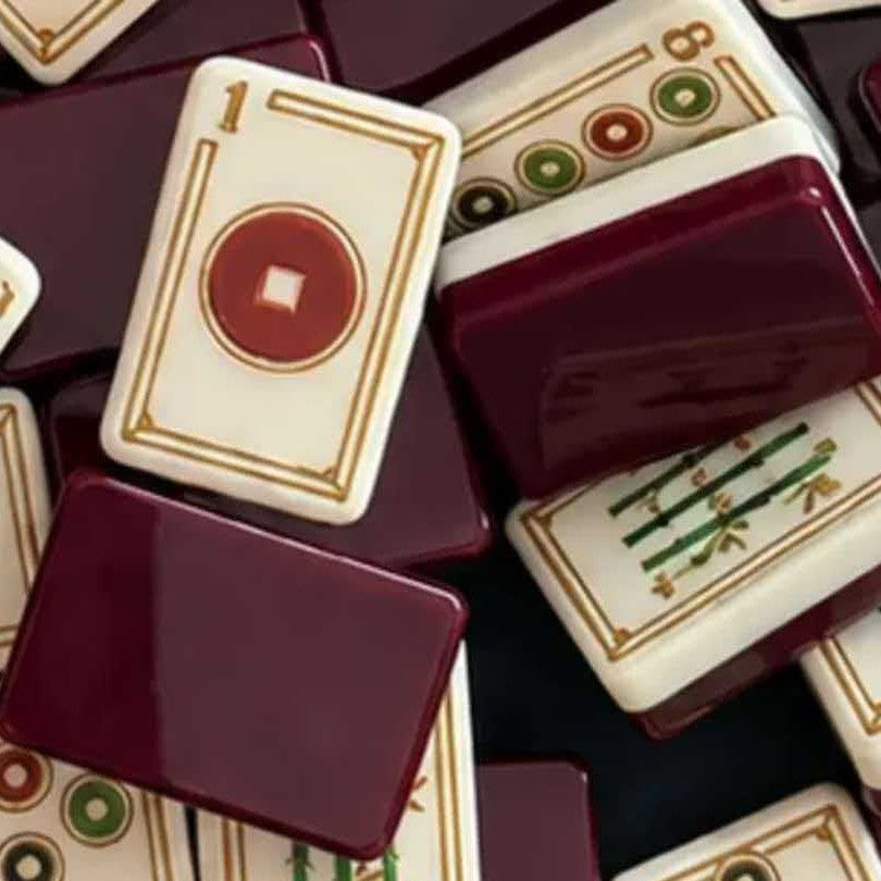 Imperial Grove mahjong overhead shot, cream dot suit tiles with vintage coin‑style artwork, solid glossy burgundy mahjong backs, premium 160‑tile American mahjong set