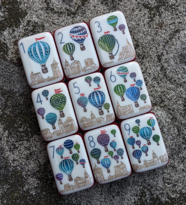 Rainbow Voyage Mahjong Tiles Set — Amber‑orange backs, multi‑layer rainbow striped sides, ivory fronts with hot‑air balloon, dragon, lantern, cherry‑blossom bee and matryoshka nesting‑doll joker American mahjong tiles