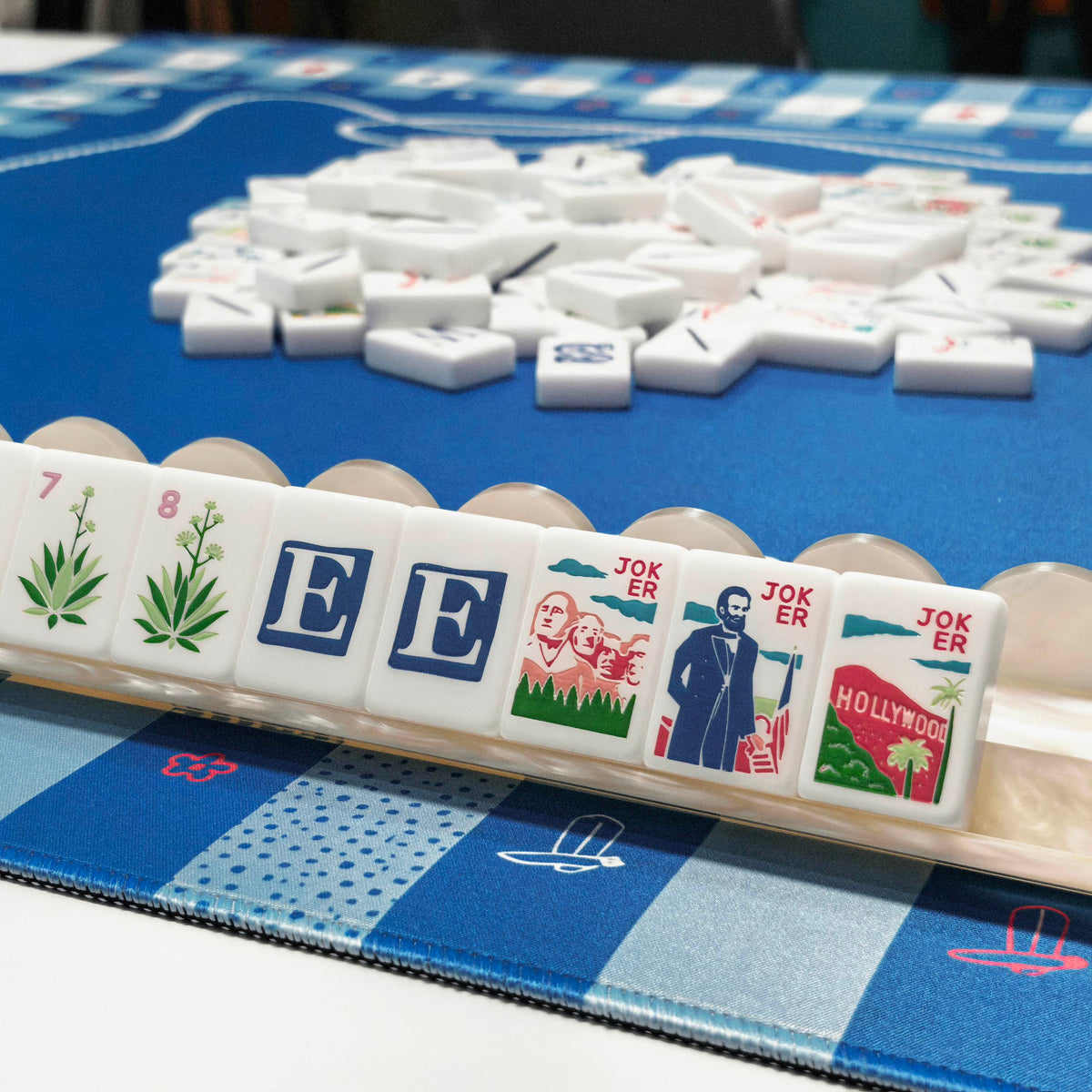 American Road Trip themed mahjong tiles arranged on tile rack on blue game mat, showing agave wind tiles and landmark jokers for mahjong game night