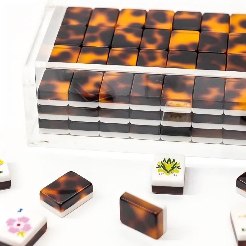 Tortoise shell mahjong tiles neatly stacked inside clear acrylic storage box, loose mahjong tiles placed on white surface to show marble tortoise back pattern