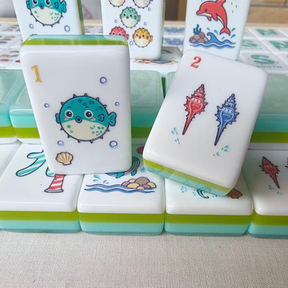 Neatly arranged Mermaid Ocean mahjong tiles with five different red-haired mermaid joker tiles in front row, lighthouse crack tile, whale tile, blue bird tile and conch shell tiles, puffer fish dot tiles at bottom
