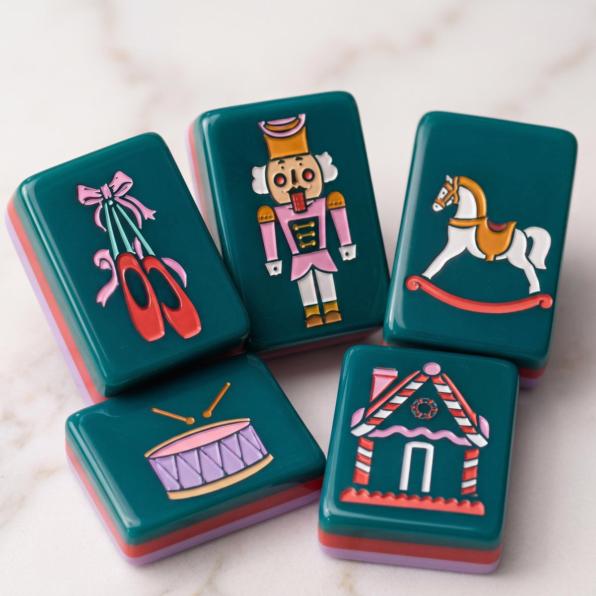 The most magical mahjong set of the season.The Holiday Nutcracker is a limited-edition collector's piece featuring rich evergreen melamine tiles adorned with hand-illustrated Christmas art from the iconic nutcracker soldier Jokers and pink ballet slipper Jokers to gingerbread house Craks, frosted cake Dots, ballerina winds (NEWS), poinsettia flowers, Christmas trees, and grandfather clocks. The ultimate holiday gift for the American Mahjong lover in your life.