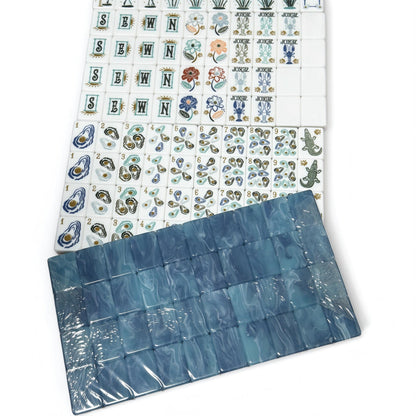 Oyster Bay coastal American mahjong set on white background, blue marbled tile backs stacked above white tile faces printed with oyster dots, heron bamboo, crab characters and alligator dragon tiles