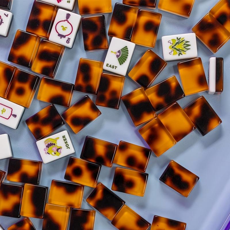 Scattered tortoise shell mahjong tiles on light blue background, featuring illustrated EAST wind tile and decorative joker tile, premium amber spotted tortoise tile backs