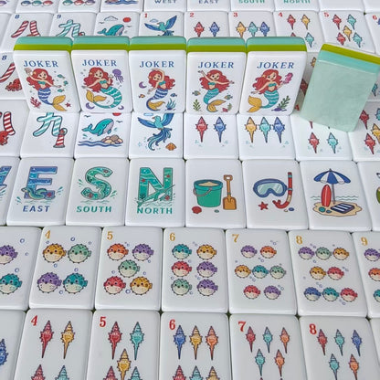 Overhead scattered shot of Mermaid Ocean mahjong tiles, showing South wind tile with seahorse, West wind with whale, North wind, ship wheel crack tiles, seahorse crack tiles, mermaid jokers and beach hut tile