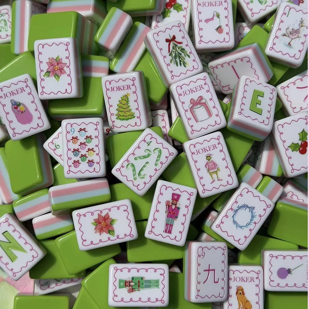 Close up pile of Christmas Grinch American mahjong tiles, featuring candy cane, nutcracker, poinsettia and Grinch joker art, green tile backs with pink white striped sides