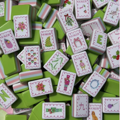Close up pile of Christmas Grinch American mahjong tiles, featuring candy cane, nutcracker, poinsettia and Grinch joker art, green tile backs with pink white striped sides