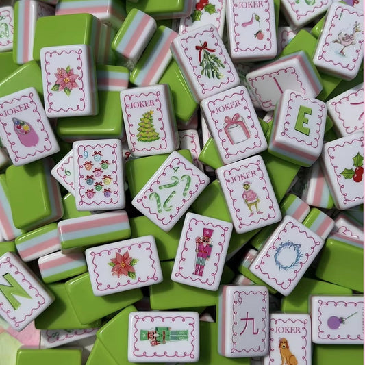 Close up pile of Christmas Grinch American mahjong tiles, featuring candy cane, nutcracker, poinsettia and Grinch joker art, green tile backs with pink white striped sides