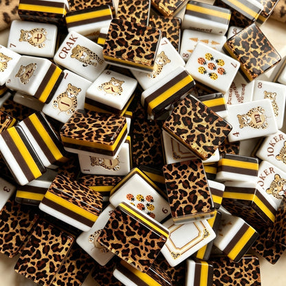 Leopard Luxe American mahjong tiles scattered flat lay, white tiles with gold pine tree, tropical bird and leopard artwork, gold glitter leopard print tile backs with yellow brown layered resin sides