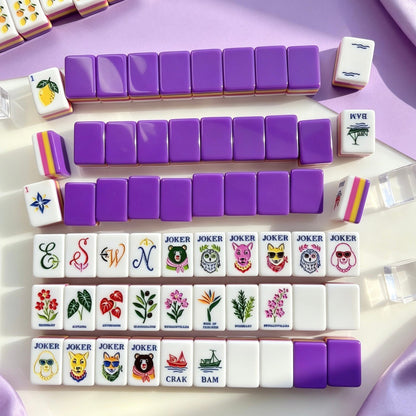 Full neatly arranged display of Purple Rainbow Striped Fruit & Fox Joker mahjong set, complete fruit, floral and animal joker tiles, styled on light stone countertop against soft purple backdrop