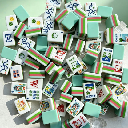 Overhead shot of scattered tropical golf resort mahjong tiles, mint green backs, pink and green striped edges, vacation themed artwork on white tile faces, styled on light green background