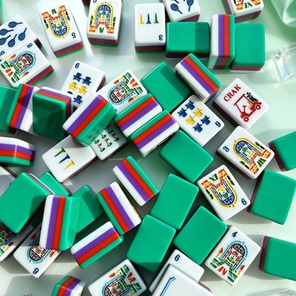 Tropical Golf Resort American mahjong tiles laid out neatly on clear acrylic tray, deep green backs, rainbow red-purple-green striped sides, custom golf and resort arch illustrations, white satin fabric backdrop