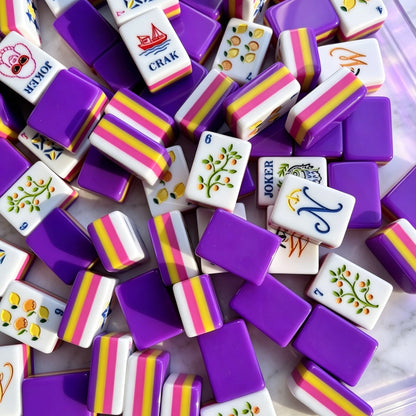 Purple rainbow striped fruit fox joker American mahjong tiles, deep purple backs with rainbow striped side layers, illustrated citrus fruit and botanical tile art, scattered on light purple background