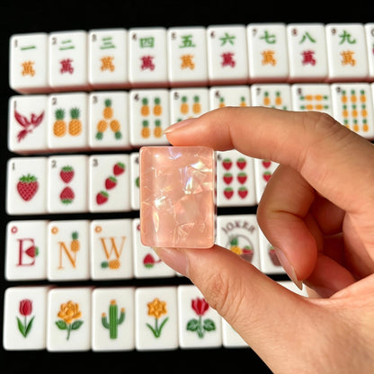 Tropical Fruit Garden American mahjong tiles scattered on marble table, pink shimmer crushed shell backs, pastel layered side stripes, strawberry and pineapple fruit illustrations, cream silk fabric backdrop