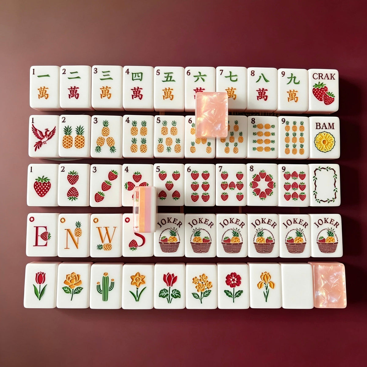 Tropical Fruit Garden American mahjong tiles scattered on marble table, pink shimmer crushed shell backs, pastel layered side stripes, strawberry and pineapple fruit illustrations, cream silk fabric backdrop