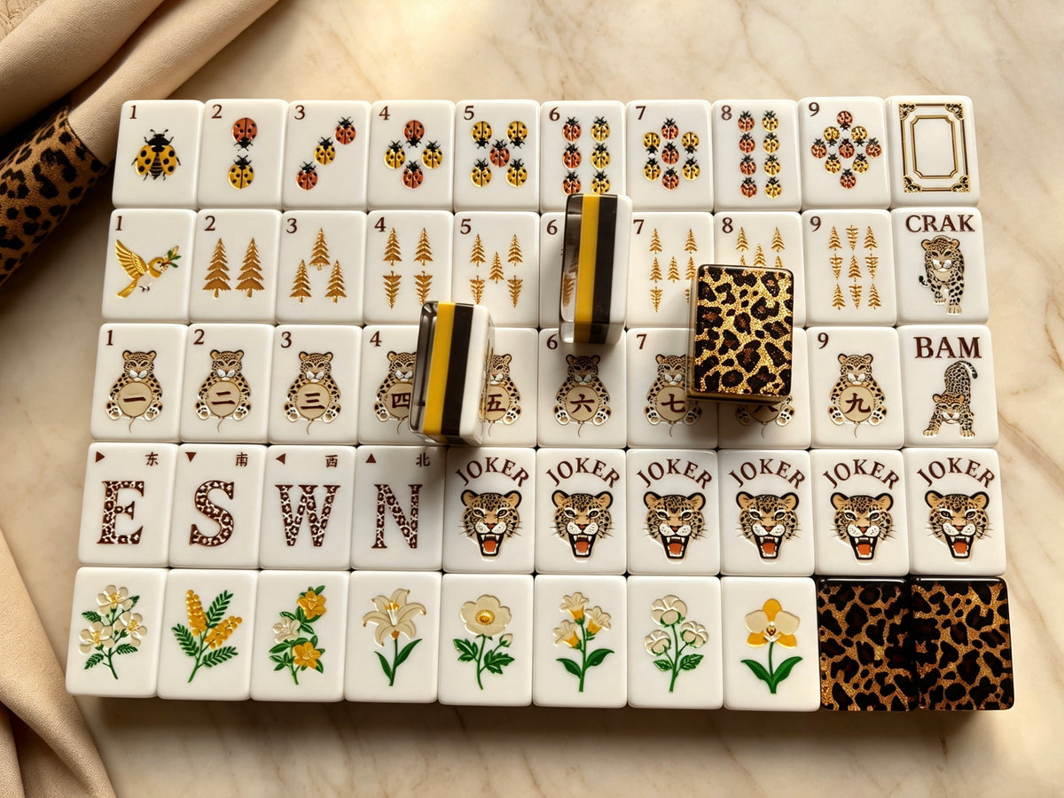 Top-down full layout of Leopard Luxe mahjong set, ladybug dot tiles, golden pine bamboo tiles, leopard character tiles, floral flower tiles and leopard face jokers on marble background