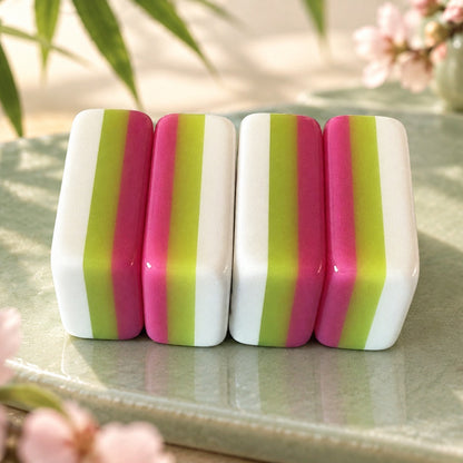 Side profile shot of neatly arranged Panda Blossom mahjong tiles, glossy fuchsia pink backs, cute panda artwork including panda jokers and scroll crak tiles, placed on embroidered green mat with sakura decor