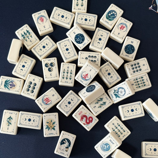 Side view of Moon Rabbit Tarot mahjong tiles lined up on acrylic rack over dark navy velvet fabric, cream ivory tiles with tarot border design, moon & star dots, floral bams, Chinese character cracks and moon rabbit lantern joker tile