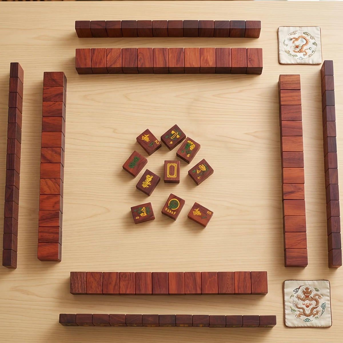 Solid red wood American mahjong set laid out for gameplay, wooden mahjong tiles with dragon embroidered coasters on light wood surface
