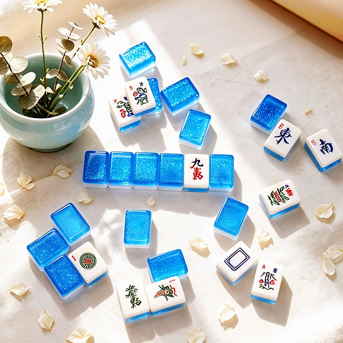 Crystal Shimmer Blue mahjong tiles arranged with daisy flowers and green vase, translucent blue glitter backs, white faces with Chinese character and wind tiles, bright sunlight American mahjong product shot