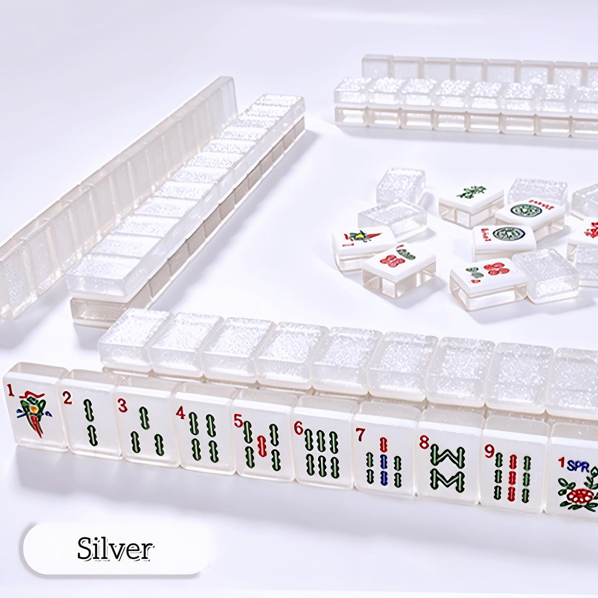 Crystal Shimmer Silver clear translucent mahjong tiles scattered on white surface, clear glitter backs, white faces with dots, bamboo, character and joker tiles, transparent acrylic American mahjong