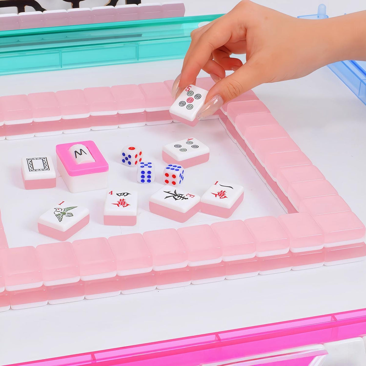 Hand picking pink Jelly Macaron translucent glossy mahjong tile during mahjong gameplay, pink mahjong wall, mahjong dice on white game table, jelly macaron style American mahjong set